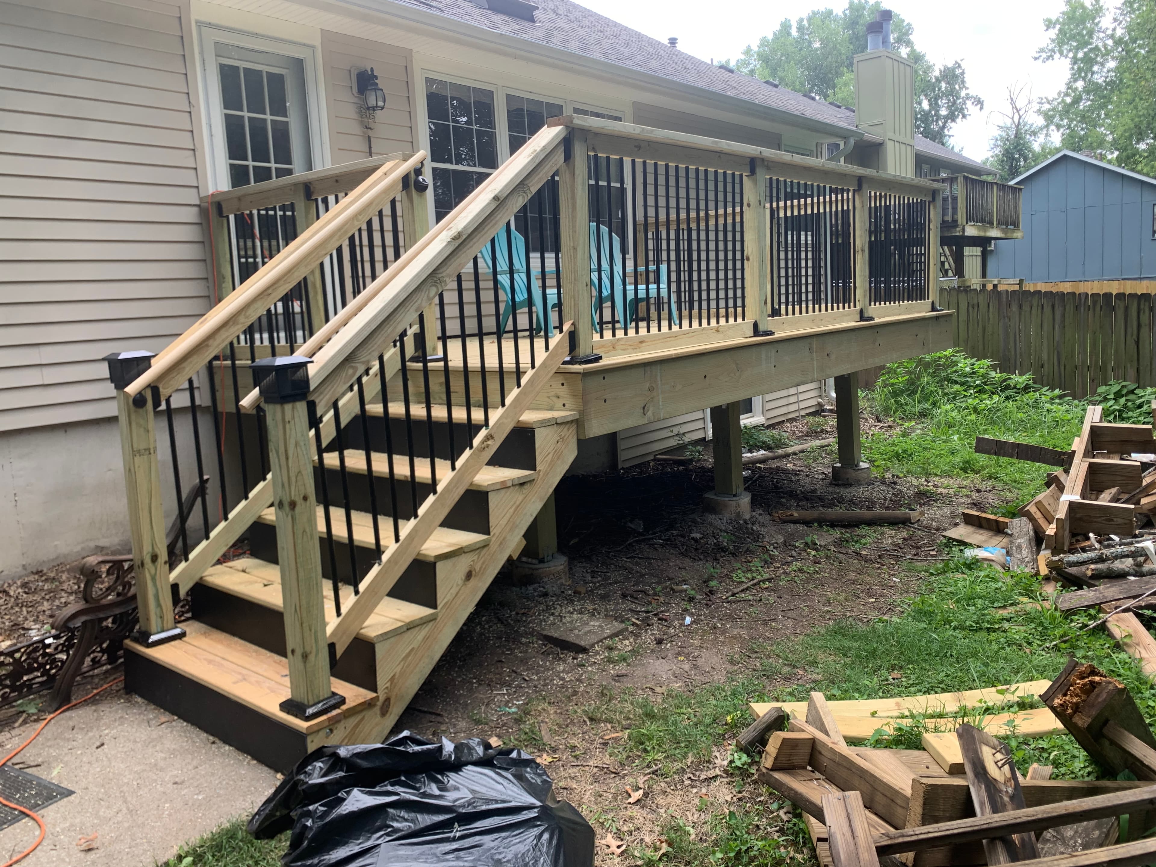 Newly constructed wooden deck with black metal railings and stairs attached to a beige house.