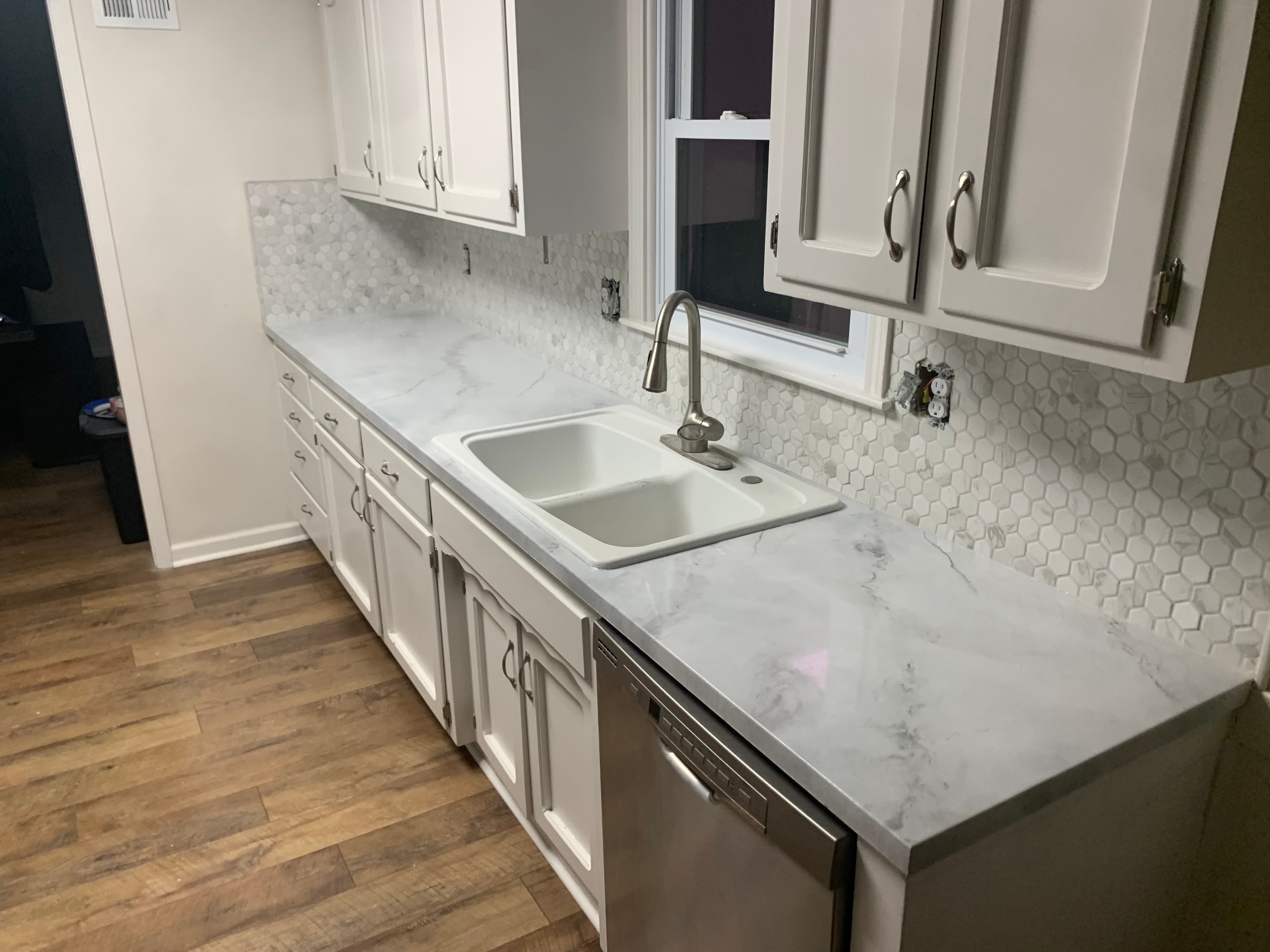 White kitchen cabinets, marble-patterned countertops, a double sink, and a white hexagonal tile backsplash.