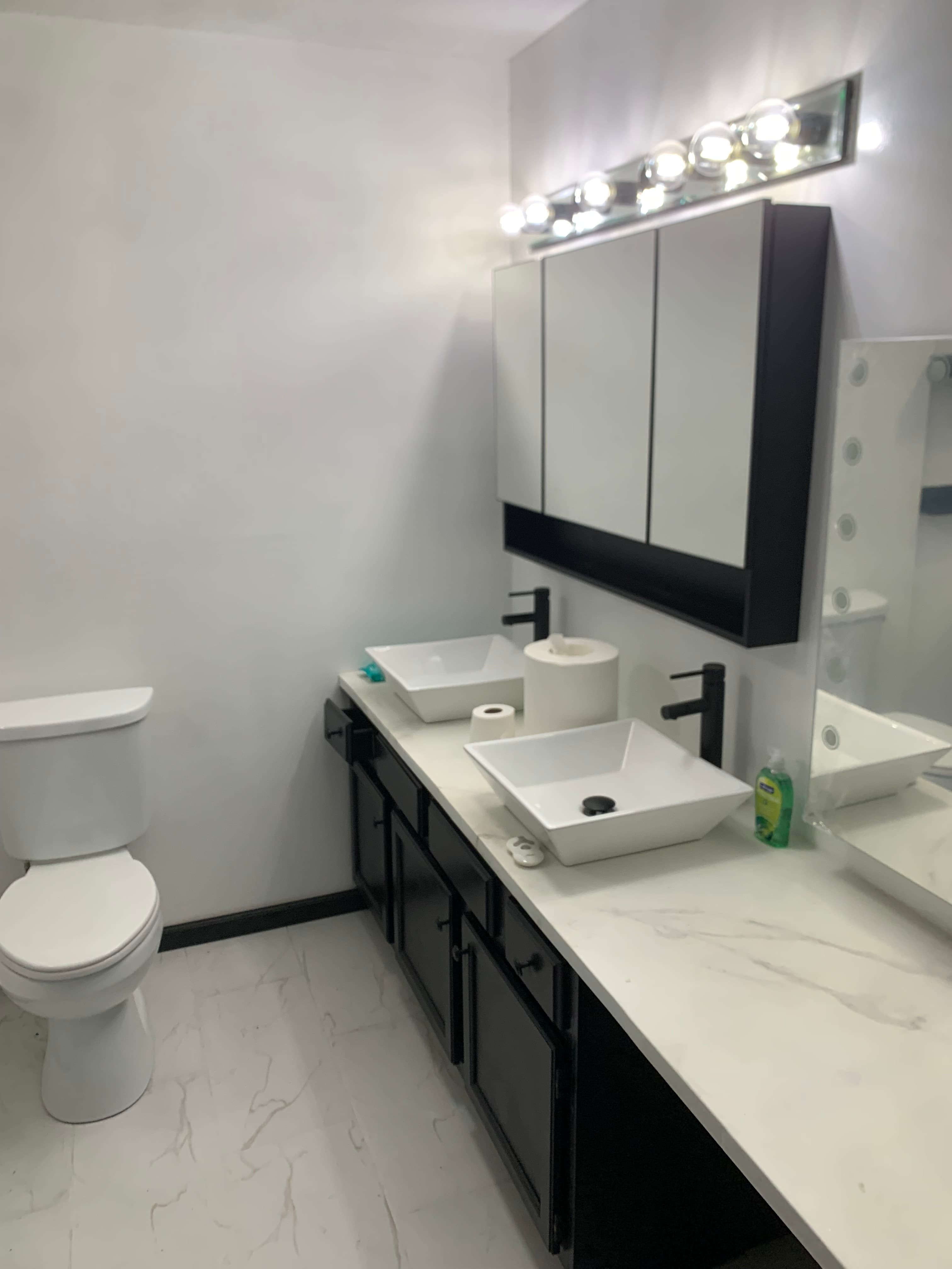 Modern bathroom featuring black vanity with double vessel sinks, white toilet, and large mirrored cabinet.