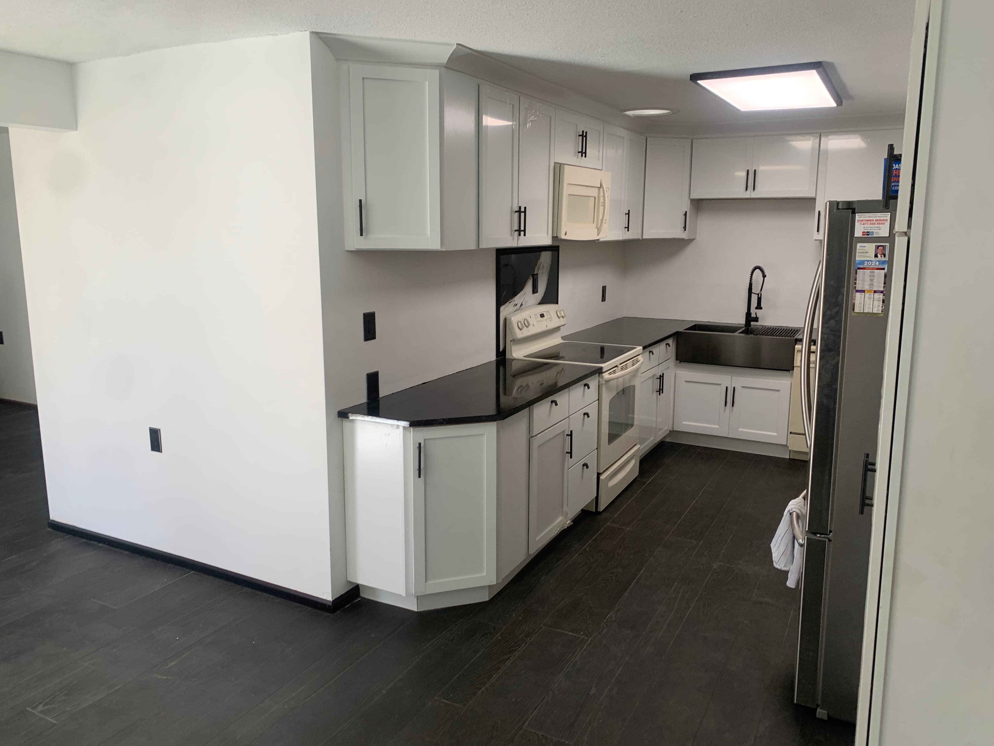 Modern kitchen with white cabinets, black countertops, dark wood floors, and stainless steel appliances.